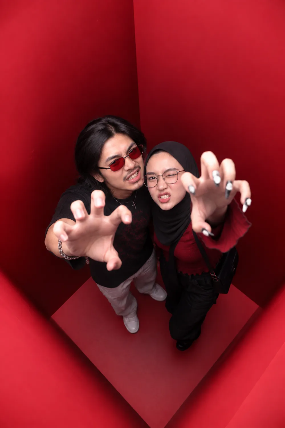 Two guests photographed from directly above inside the red booth, both stretching their hands up towards the camera.