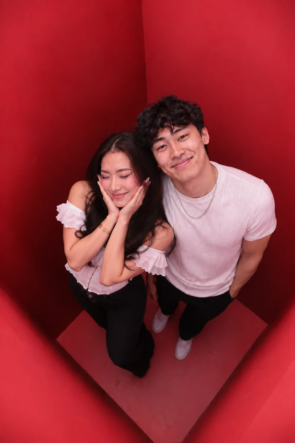 Two guests photographed from directly above inside the red booth, one resting her cheek on her hands while the other leans in behind her.