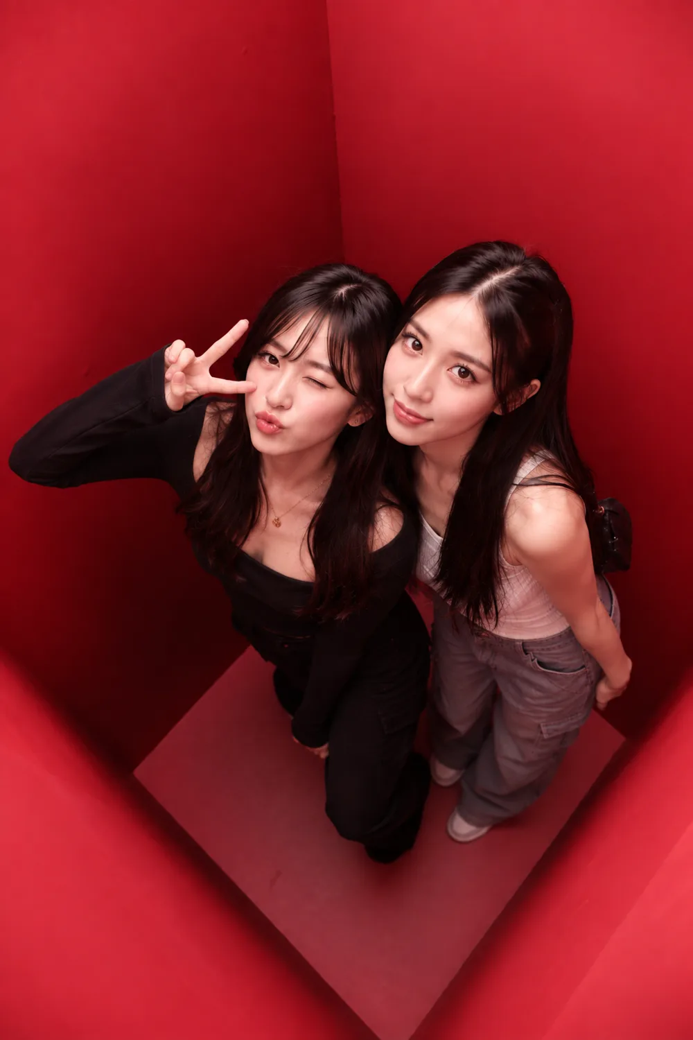 Two guests photographed from directly above inside the red booth, standing close together with one raising a peace sign.