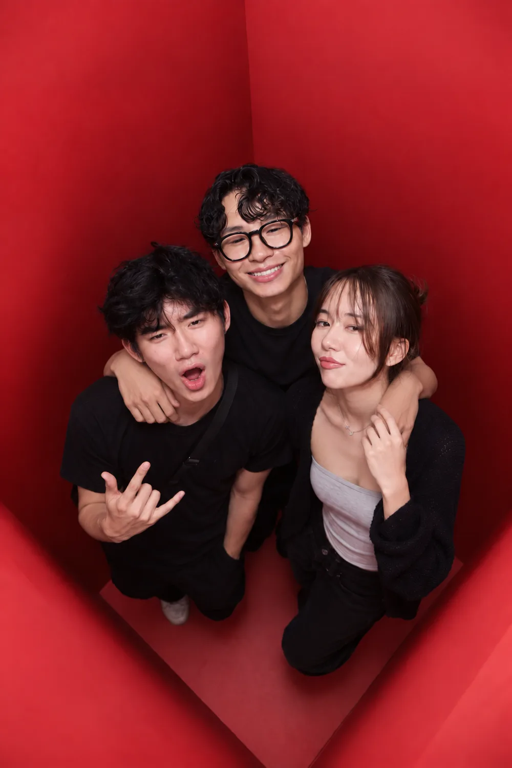 Three guests photographed from directly above inside the red booth, arms around each other and hand signs raised to the camera.