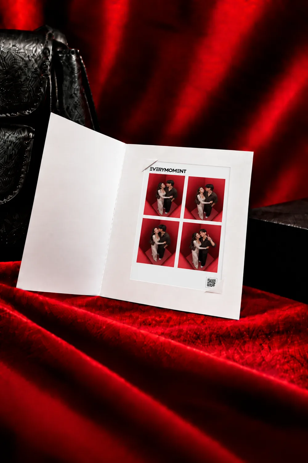 A white folded card opened on red velvet to show a strip of four photographs from the booth, with the EVERYMOMENT wordmark and a QR code beside them. A black handbag sits behind it.