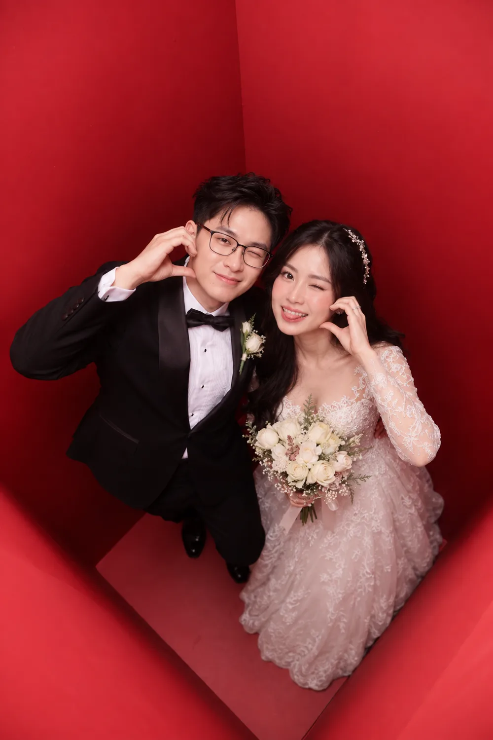 A couple in wedding dress photographed from directly above inside the red booth, the bride holding a bouquet and both looking up at the camera.