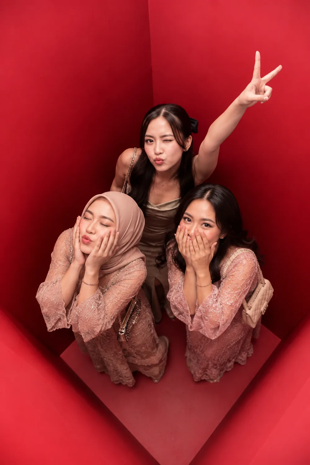 Three guests in lace formal dress photographed from directly above inside the red booth, two crouching and one standing with a raised hand.